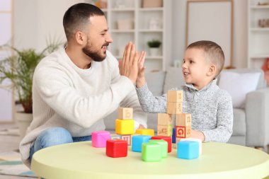 Mutlu baba ve küçük oğlu odada renkli küplerle oynarken birbirlerine beşlik çakıyorlar.