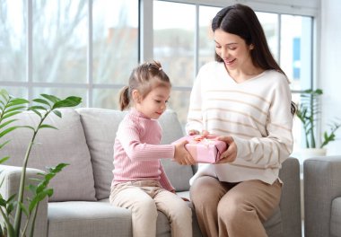 Genç anne ve hediye kutusuyla evdeki kanepede oturan küçük kızı.