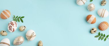 Açık mavi arkaplanda boyanmış Paskalya yumurtaları ve yaprakları yazı için yer, üst görünüm
