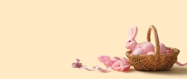 Boyanmış Paskalya yumurtaları, oyuncak tavşancık ve bej arka planda lale çiçekleri olan hasır sepet.