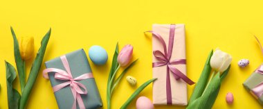Lale çiçekli Paskalya yumurtaları ve sarı arka planda hediye kutuları.
