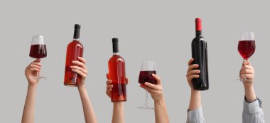 Şişeli kadın elleri ve gri arka planda kırmızı şarap bardakları.