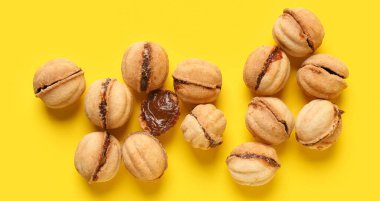 Sarı arka planda kaynamış yoğunlaştırılmış sütle pekçok tatlı ceviz şekilli kurabiye.