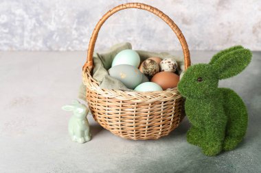 Paskalya yumurtası ve tavşanlı sepet grunge duvarının yanındaki masada.