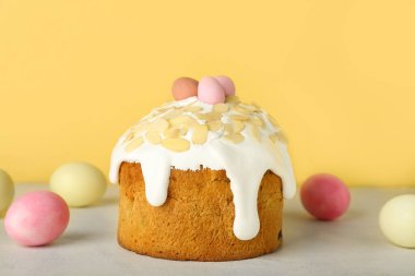 Easter cake and painted eggs on table near yellow wall