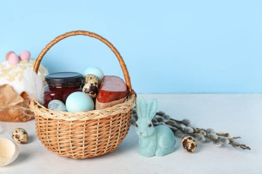 Paskalya yumurtalı sepet, jambon ve tavşancık gri masada mavi arka planda.