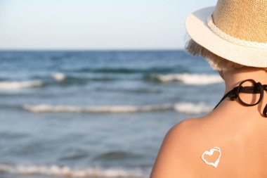 Deniz kıyısında genç bir kadının sırtına güneş kremiyle çizilmiş bir kalp.