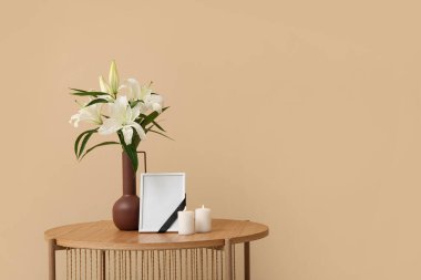 Boş cenaze çerçevesi, yanan mumlar ve vazo, ahşap masa üzerinde zambak çiçekleri, renk duvarının yanında.