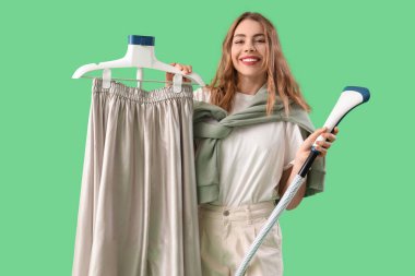 Yeşil arka planda modern giysi buharı olan güzel genç bir kadın.