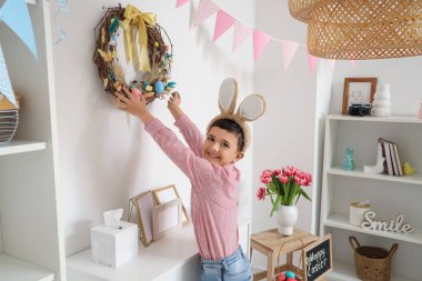 Tavşan kulaklı şirin çocuk Paskalya çelengiyle oturma odasını dekore ediyor.