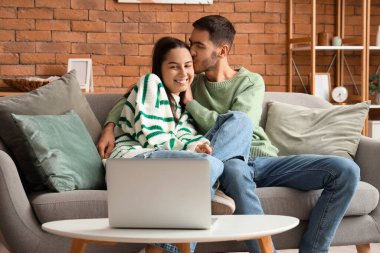 Evdeki kanepede dizüstü bilgisayarı olan genç ve güzel bir çift.