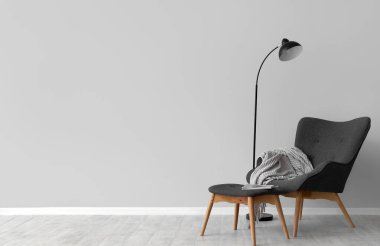 Gri duvarın yanında koltuk, ayak sehpası ve lamba olan oturma odasının içinde.