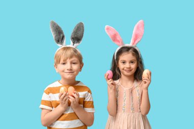 Mavi arka planda Paskalya yumurtaları olan tavşan kulaklı şirin bir çocuk.