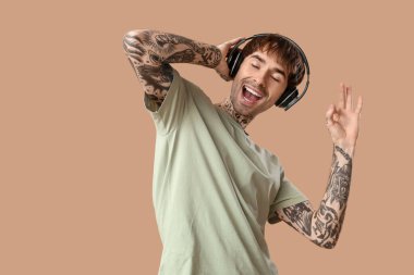 Kulaklıklı genç dövmeli adam bej arka planda dans ediyor.