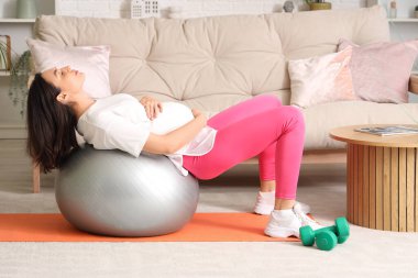 Güzel, genç, hamile bir kadın evde fitbol antrenmanı yapıyor.