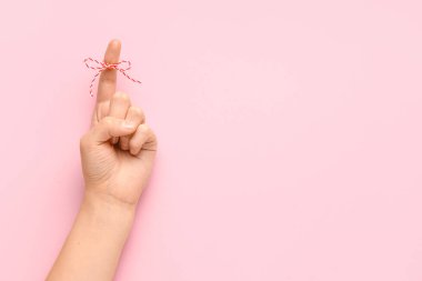 Pembe arka planda işaret parmağında kırmızı fiyonk olan bir kadın el. Hatırlatma konsepti