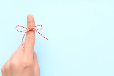İşaret parmağında kırmızı fiyonklu kadın eli mavi arka planda. Hatırlatma konsepti