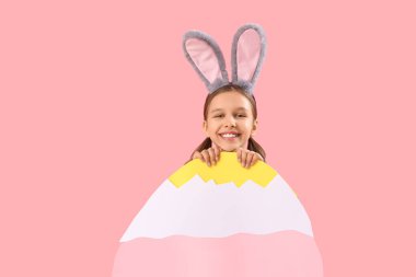 Paskalya tavşanı kulakları ve pembe arka planda büyük kağıt yumurtası olan tatlı küçük bir kız.