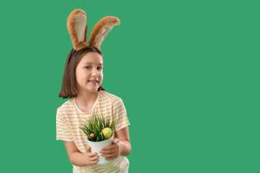 Paskalya tavşanı kulaklı tatlı küçük kız ve yeşil arka planda saklı yumurtaları olan bitki.