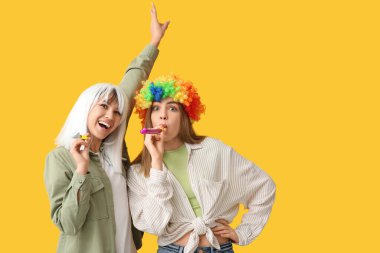 Sarı arka planda parti düdükleriyle komik kılık değiştirmiş güzel genç kadınlar. 1 Nisan şakası