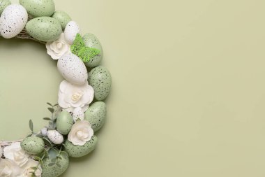 Beyaz çiçekli Paskalya çelengi, açık yeşil arka planda yumurta ve kelebekler.