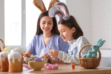 Küçük kız ve annesi tavşan kulaklı mutfakta Paskalya çelengi yapıyorlar.