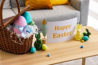 Paskalya yumurtalı sepet, oyuncak tavşanlar ve oturma odasındaki masada tebrik kartı.