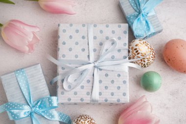 Hediye kutularıyla boyanmış Paskalya yumurtaları ve beyaz grunge arka planda lale çiçekleri.