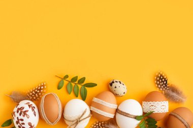 Süslü Paskalya yumurtaları, tüyleri ve sarı arka planda yaprakları olan kompozisyon
