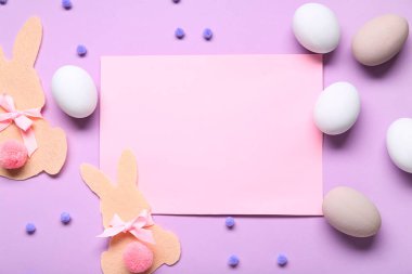 Paskalya yumurtaları, keçeli tavşanlar ve leylak arka planda boş tebrik kartı. Üst görünüm