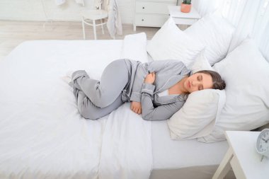 Pijamalı genç bir kadın evde yatakta uyuyor.