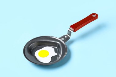 Kalp şeklinde kızartma tavası ve mavi arka planda kızarmış yumurta.