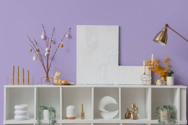 Söğüt dallı vazo, Paskalya yumurtası ve eflatun duvarın yanındaki raflarda resimler.