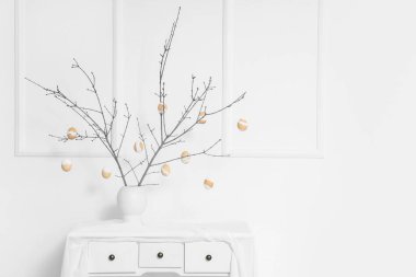 Ağaç dalları ve Paskalya yumurtaları olan vazo ışık duvarının yanında.