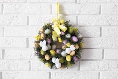 Beyaz tuğla duvarda yumurtalarla süslenmiş güzel Paskalya çelengi.