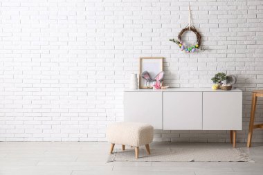 Güzel Paskalya çelengi beyaz tuğla duvarda yumurtalarla süslenmiş şık bir odada çekmecelerin yanında.