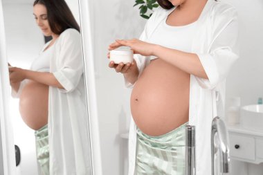 Banyoda bir kavanoz kremalı hamile kadın, yakın plan.
