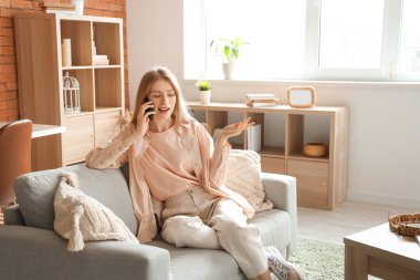 Oturma odasındaki koltukta cep telefonuyla konuşan genç ve güzel bir kadın.