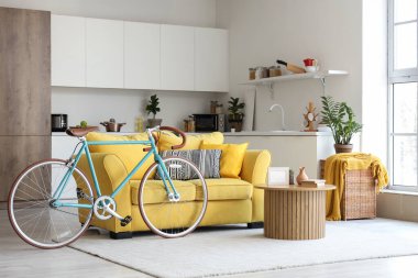 İçinde sarı kanepe, sehpa, tezgah ve bisiklet olan güzel bir oturma odası.