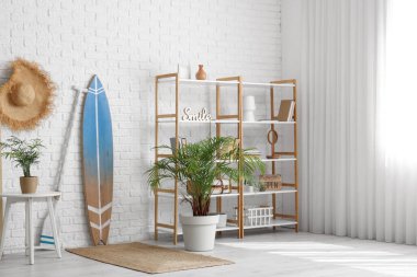 Beyaz tuğla duvarın yanında sörf tahtası ve raf ünitesi olan modern tarz bir oda.