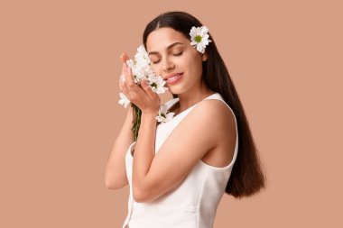 Bej arka planda papatya çiçekleri olan güzel, genç bir kadın.