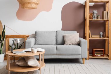 Gri kanepesi, raf ünitesi ve masası olan rahat bir oturma odası.