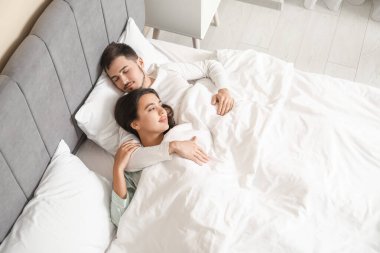 Kocasıyla yatak odasında battaniyenin altında uyuyan genç bir kadın.