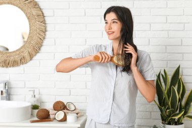 Güzel genç bir kadın banyodaki saçlara hindistan cevizi yağı sürüyor.