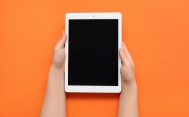 Turuncu arka planda tablet bilgisayarlı kadın elleri