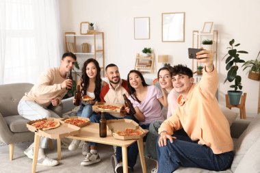 Biberli pizza ve birayla mutlu arkadaşlar evde selfie çekiyorlar.
