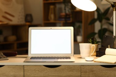 Karanlık ofisteki masasında parlak lamba olan boş bir laptop.