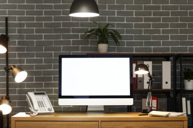 Boş bilgisayar monitörü ve parıldayan lamba karanlık ofisteki masada.