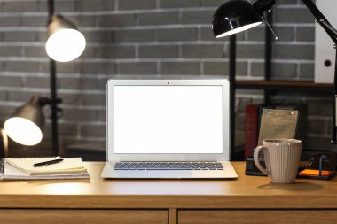 Karanlık ofisteki masasında parlak lamba olan boş bir laptop.