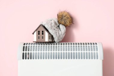 Pembe arka planda, ısıtıcı takılı sıcak şapkalı ev modeli. Isıtma kaydetme kavramı